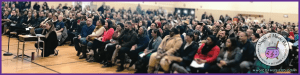 Elementary music teacher engaging with a large audience of parents at a school concert, fostering parent-teacher relationships and a supportive music community.