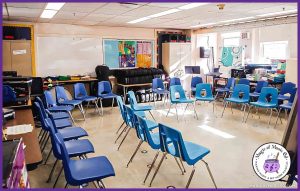 Elementary chorus classroom setup with blue chairs arranged in a semi-circle, music posters on the walls, and instrument storage in the background.