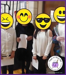 Elementary chorus students standing together, holding programs before a school concert, dressed in white and black attire.