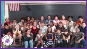 Group photo of an elementary chorus class sitting on risers during a school rehearsal, with students blurred for privacy.