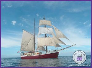 A majestic sailing ship with its sails fully open against a bright blue sky, symbolizing adventure and life at sea. This image represents the Songs from the Sea choir concert theme.