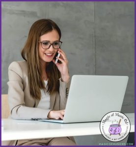 A smiling music teacher in a beige blazer sits at a desk, talking on the phone while working on her laptop. The Magic of Music Ed logo is in the bottom corner, representing positive communication in music class.
