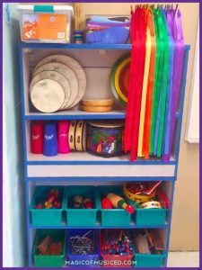 Colorful general music supplies on a classroom shelf, including hand drums, ribbon wands, and percussion instruments, organized in bins for elementary music teachers managing a tight classroom budget.