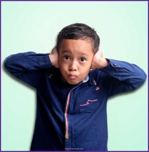 Young child covers ears with a silly face, showing a playful reaction to loud sounds—perfect for introducing loud and soft dynamics in kindergarten music class.