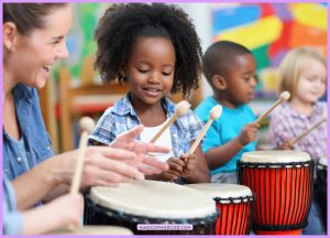 A teacher and elementary students play hand drums in a colorful classroom, showing music education and music education benefits in action.