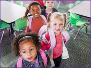 Kindergarten students line up in the classroom with backpacks, smiling and ready for music class.