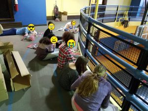 Elementary students sitting on the floor preparing music books for band class, showing the challenge of starting an elementary band with no instruments.